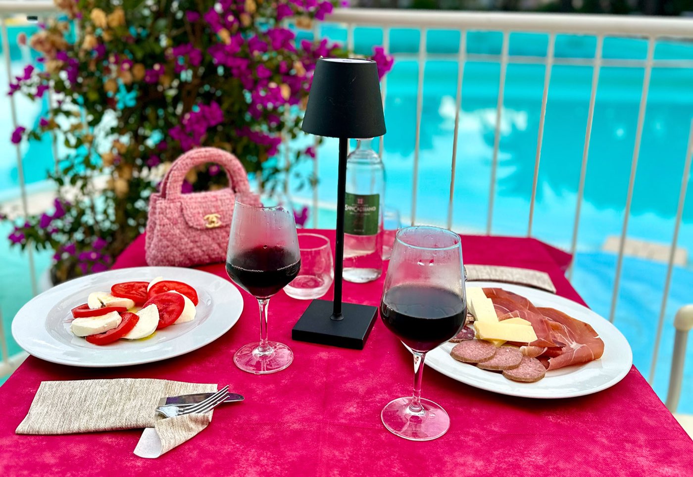 Tavolo apparecchiato a bordo piscina con vino rosso e antipasti